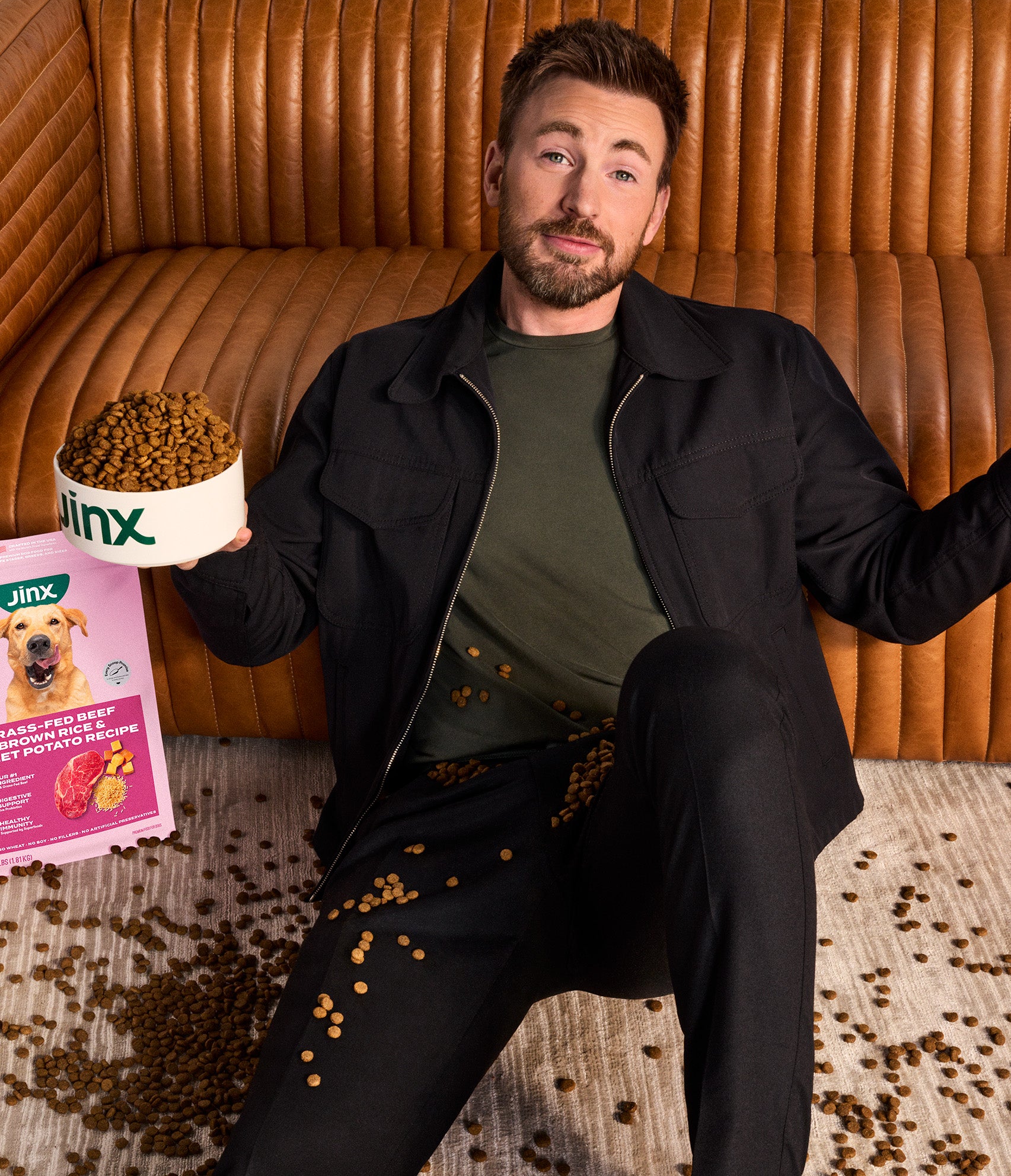 an image of Chris Evans sitting on the ground shrugging, covered in Jinx kibble.