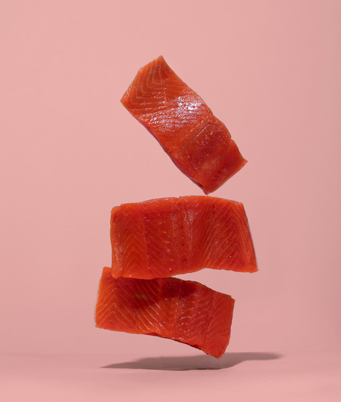 Salmon slices artistically hovering in the air on a pink background