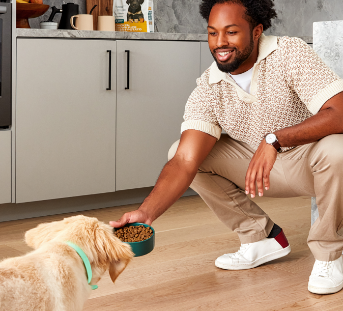 Man crouching down holding out a bowl of dog food and a puppy running up to the bowl