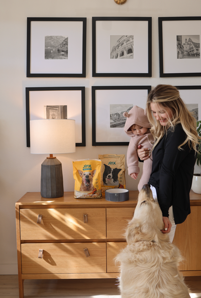 Woman holds baby while feeding dog