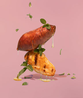 Sweet potatoes dripping in honey with mint, artistically hovering in the air on a pink background