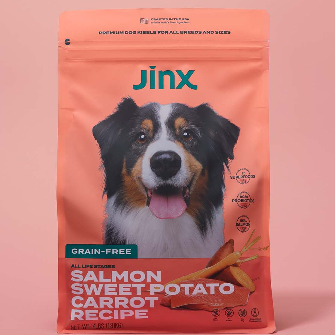 Grain-free salmon essentials Jinx bundle including Salmon, sweet potato & carrot dog kibble product packaging on a pink background.