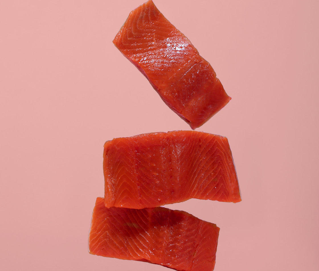Salmon slices artistically hovering in the air on a pink background